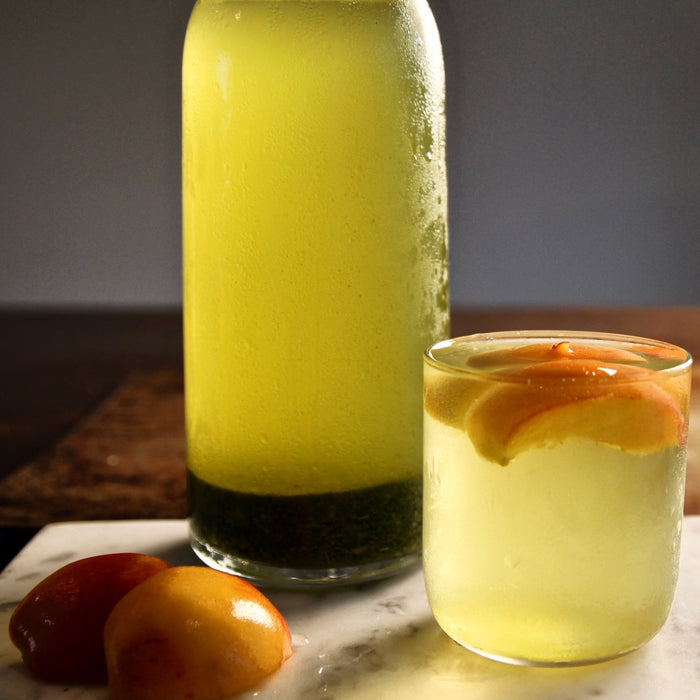 Carafe and glass of cold brew sencha with frozen peach garnish
